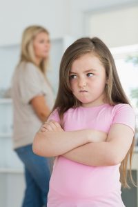 Little girl looking angry in the kitchen with mother in background