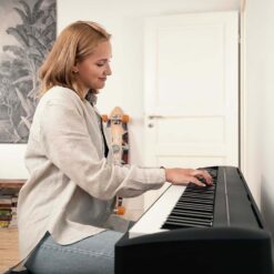 Image of woman in white sweater playing a Kawai ES120BK digital piano in her home