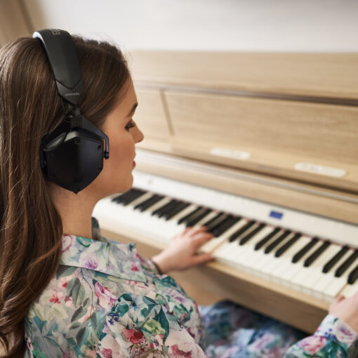 Image of woman playing a Roland LX-5 in Light Oak, with Roland Headphones on